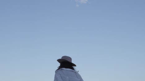 young woman girl with hat and white shirt on, blue sky background walking