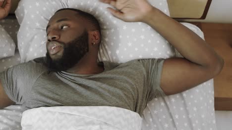 hombre negro acostado en la cama. hombre enojado despertando en el dormitorio