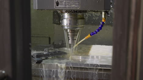 coolant spray and metal shavings fly as cnc machine drills into metal at a workshop