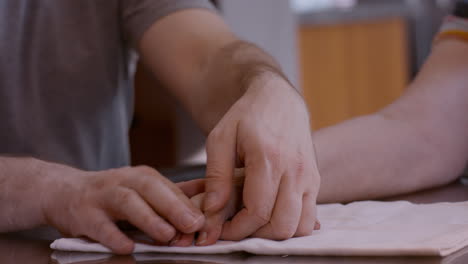 middle-aged male caregiver assists female stroke survivor by gently stimulating and mobilizing fingers of her hemiplegic right hand during a therapy session at home kitchen table on cloth pad. 24fps.