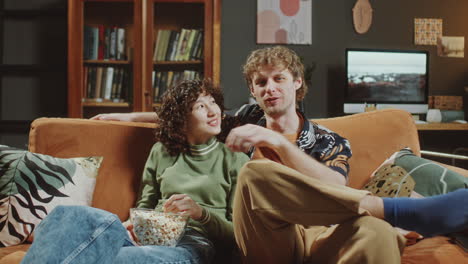 young couple eating popcorn and watching movie in cozy living room