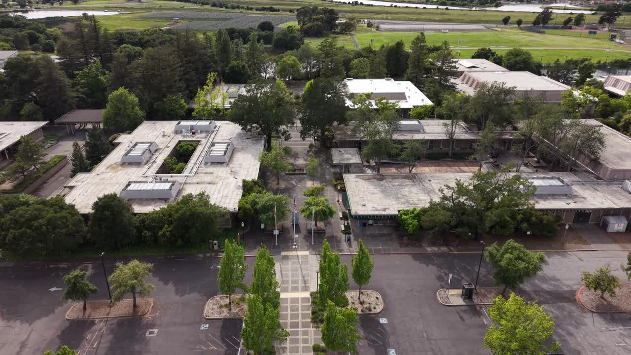 Vista aerea con drone in ascesa che vola all'indietro sopra gli edifici del campus del Napa Valley College, i parcheggi e i vialetti, rivelando lo splendido paesaggio verde circostante della California settentrionale.