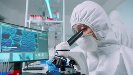 enfermera en traje de ppe haciendo experimentos médicos usando el microscopio