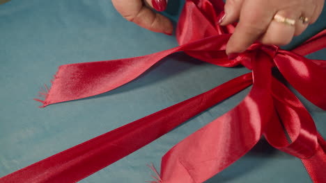 manos de una mujer atando un arco de cinta roja en una caja de regalo