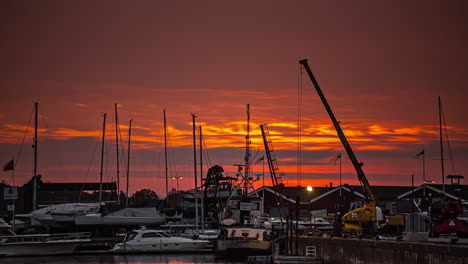 time lapse shot of red sunrise at port with docking sailing boats and working industrial crane at harbor in the morning