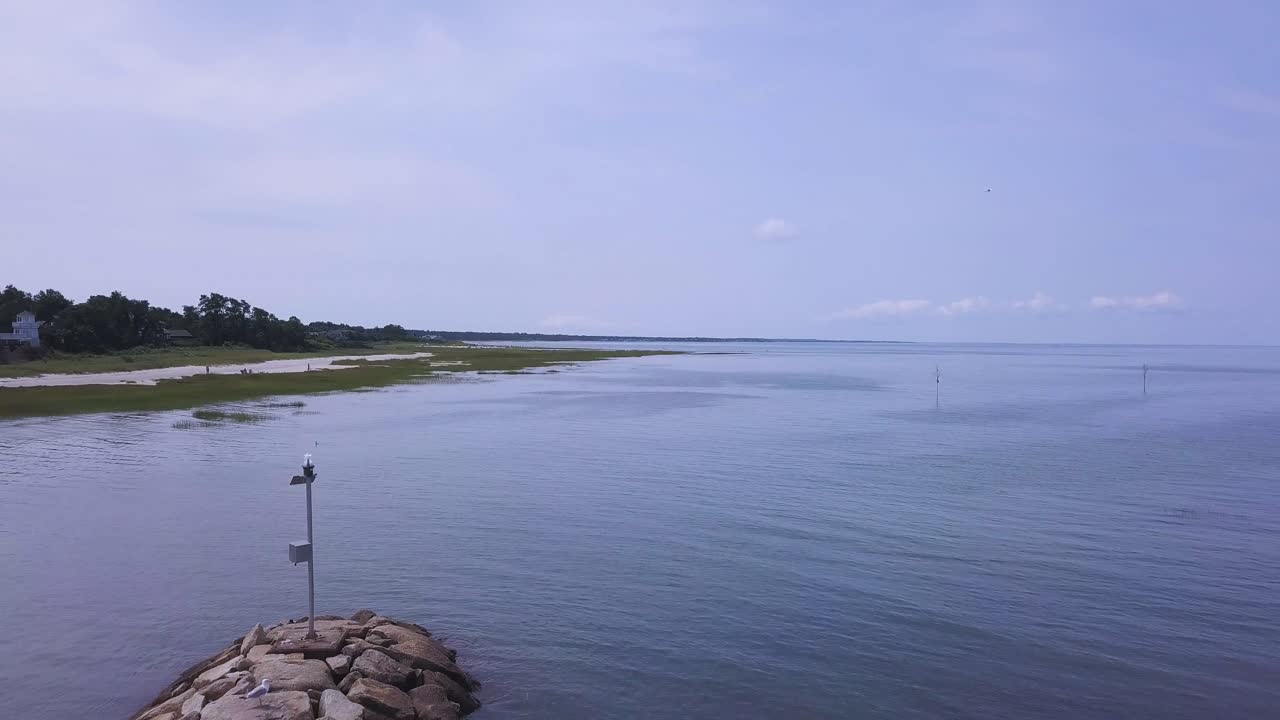 The camera pulls back and reveals the breakwater. You can see the vast expanse of the bay. Seabirds can be seen flying through the frame, and people are walking the shoreline.