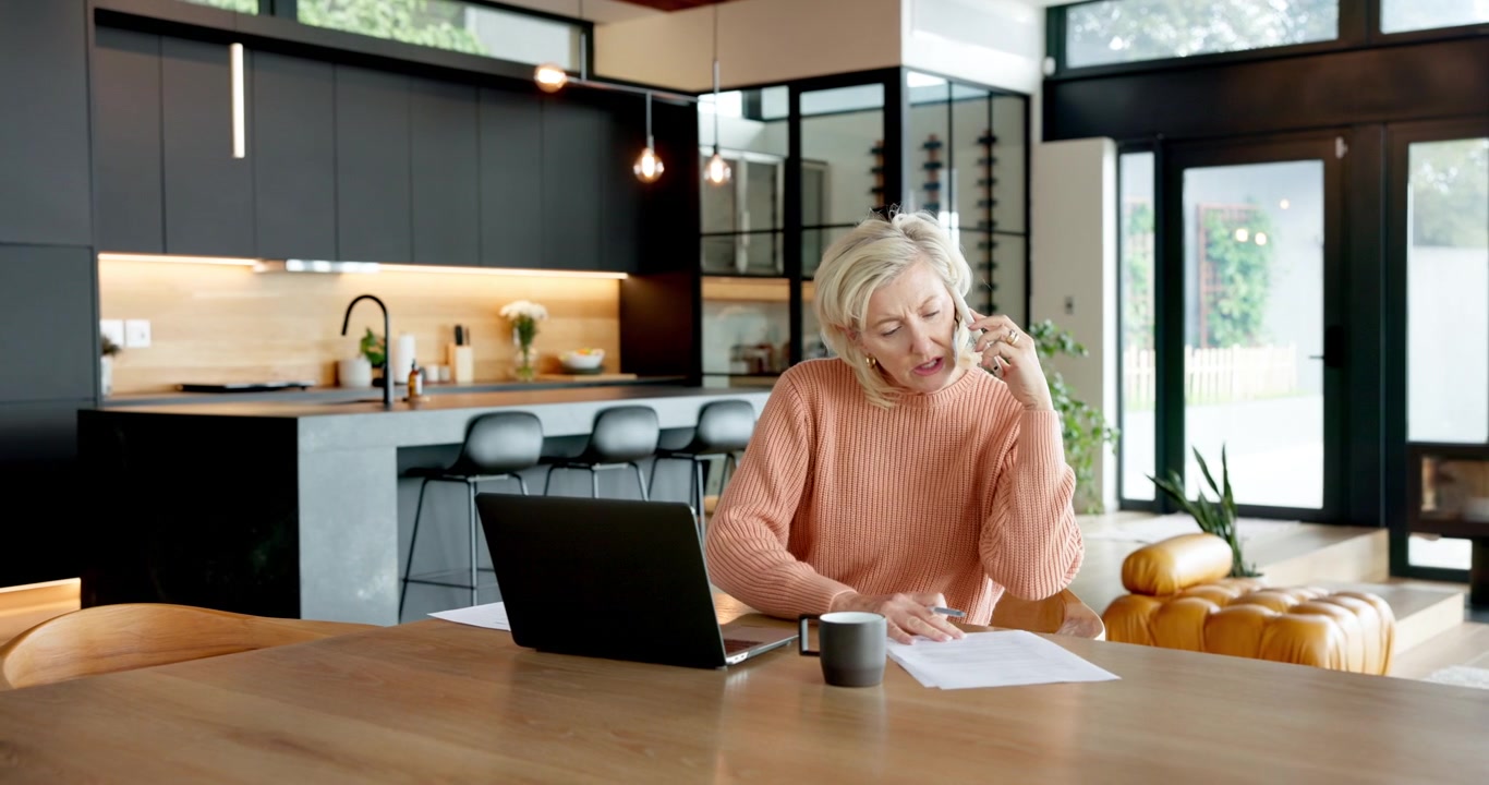 Mature Woman Working on Laptop and Talking on Phone at Home