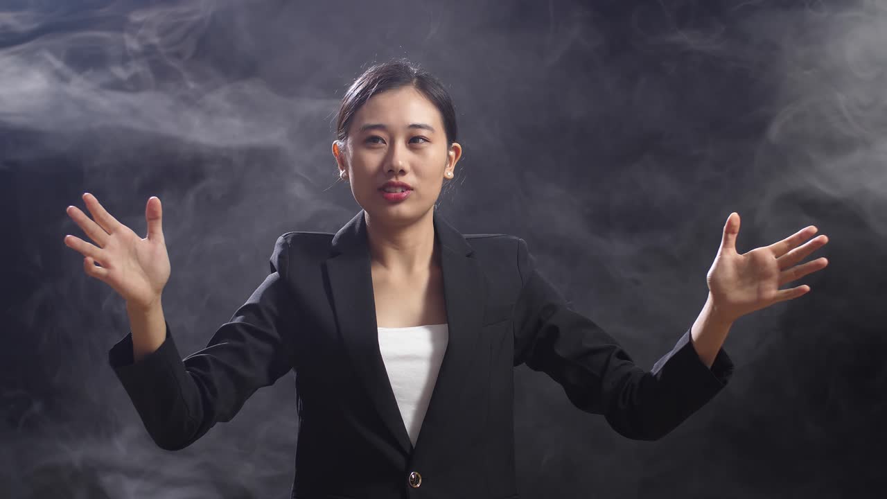 블랙 스크린 스튜디오 에서 연설 하는 동안 손 을 고 있는 비즈니스 슈트 를 입은 아시아 여성
