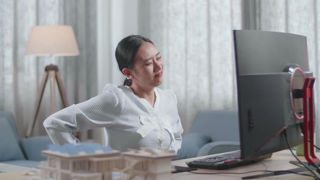 ingeniera asiática con el modelo de casa con dolor de espalda mientras trabaja en un escritorio en casa