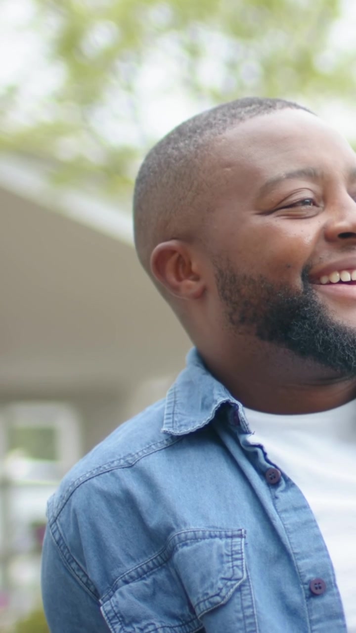 Vertical video: Smiling man in denim shirt laughing on bench while camera panning, revealing watch
