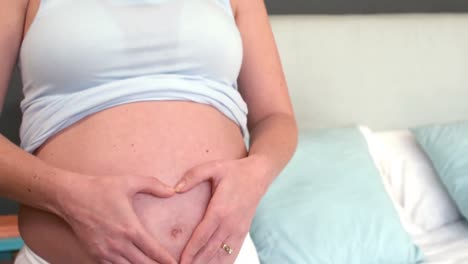 pregnant woman putting hands on belly making heart