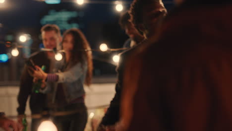 happy group of friends dancing together enjoying rooftop party music at night having fun drinking alcohol celebrating weekend reunion gathering