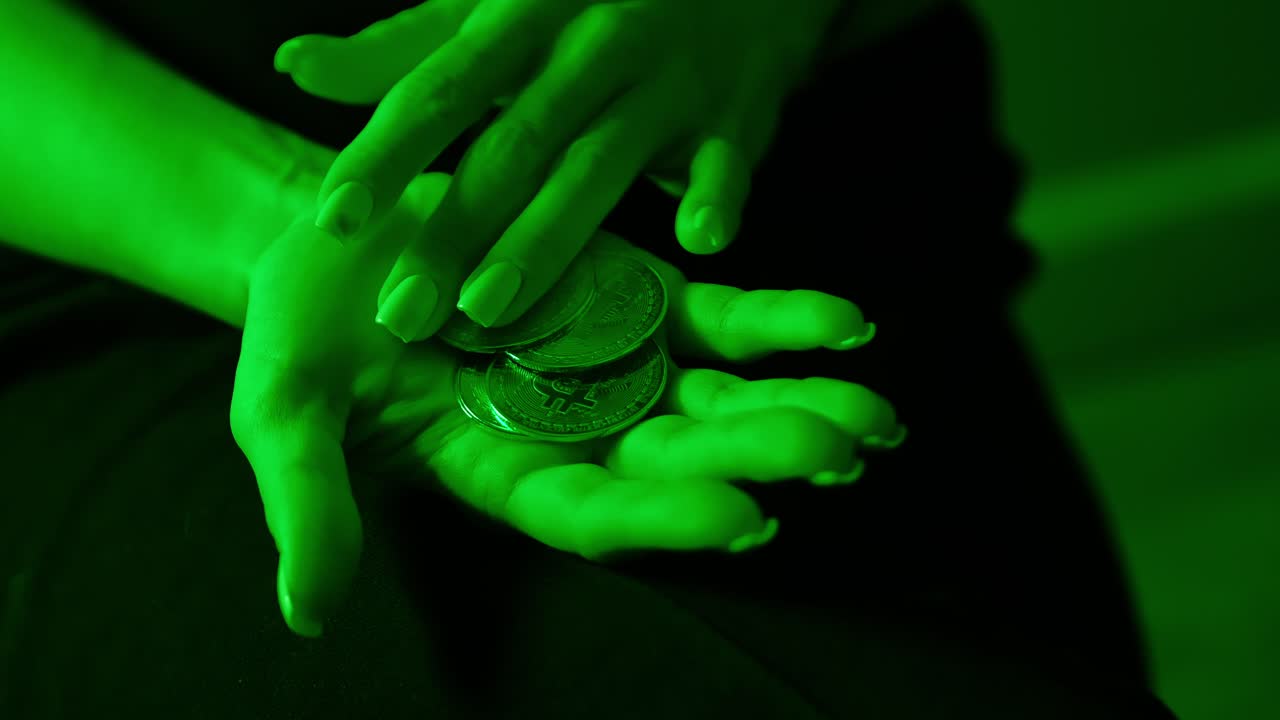 Woman slowly arranges shiny Bitcoin tokens across her palm in green glow