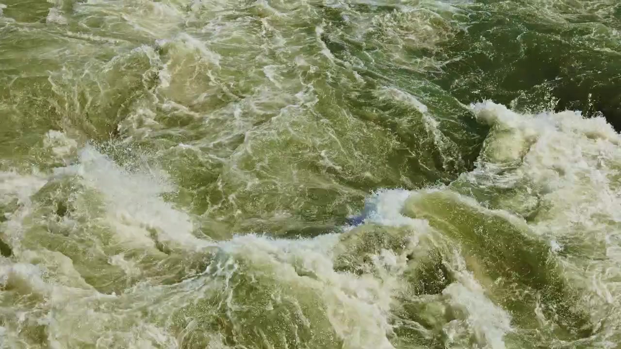 Woda płynie, tworząc fale i zmarszczki, w ciągu dnia, w blasku słońca, w pobliżu brzegu rzeki lub plaży.