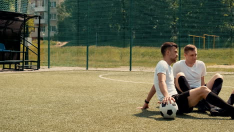 young street football players sitting on pitch, resting and talking to each other on a sunny day