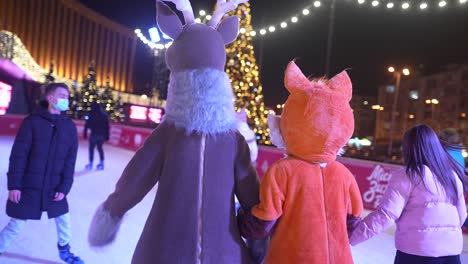 niños con trajes de ciervo y zorro patinando sobre hielo por la noche