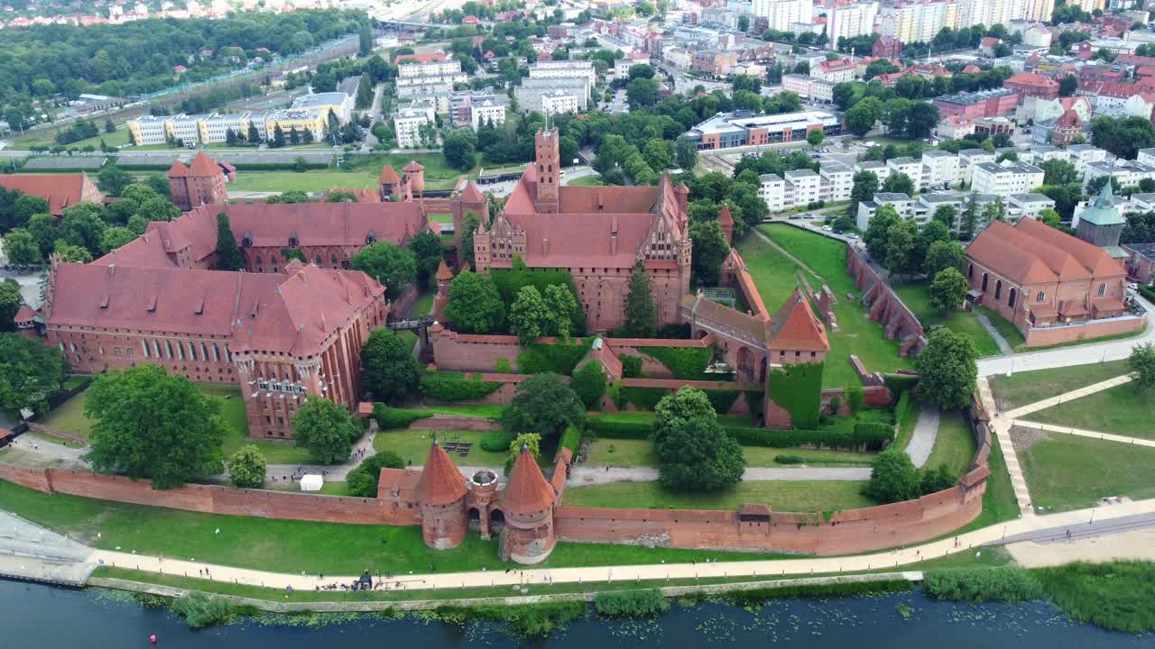 Drone footage over Malbork Castle, medieval red-brick architecture and lush surroundings. Malbork, Poland