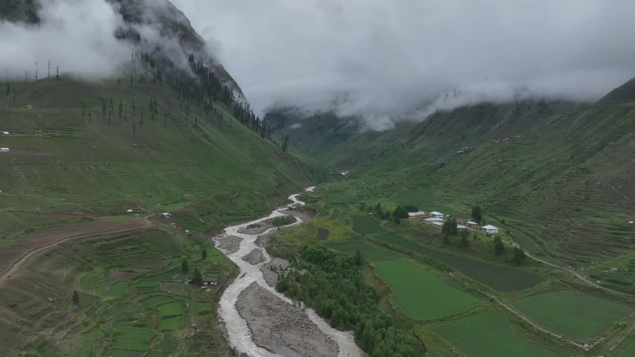 Accending and then follow drone shot over the calming lake and lush green valley in Northern area of Pakistan on a cloudy day