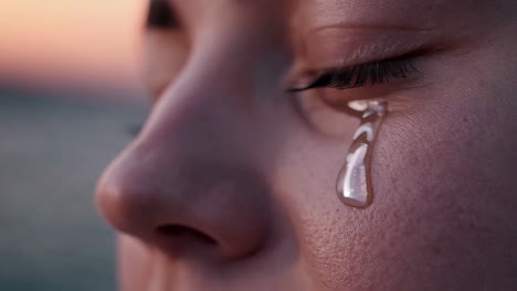close-up of a person's face with a tear streaming down at sunset