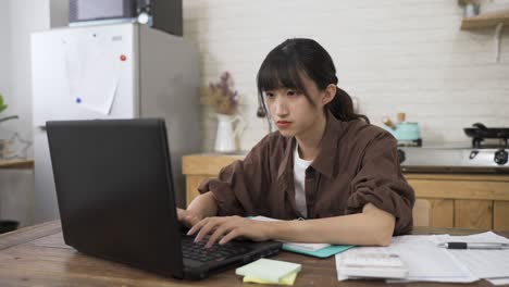집중된 아시아 여성 직원의 초상화는 낮에 식당에서 컴퓨터에서 집에서 타이핑하고 있습니다.