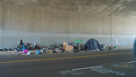 Campamento-Para-Personas-Sin-Hogar-Bajo-Un-Paso-Elevado-Con-Pertenencias-Personales-Esparcidas-Por-Todos-Lados,-Luz-Del-Día