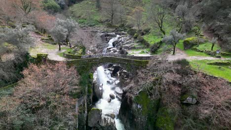 Orbit-shot-over-Scenic-Medieval-stone-brigde,-Mizarela-Bride-surrounded-by-greenery-landscape,-Portugal