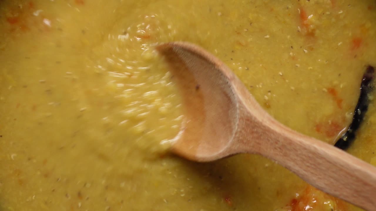 fotografía de cerca de una olla de dal, una popular sopa de lentejas indias, siendo agitada con una cuchara de madera