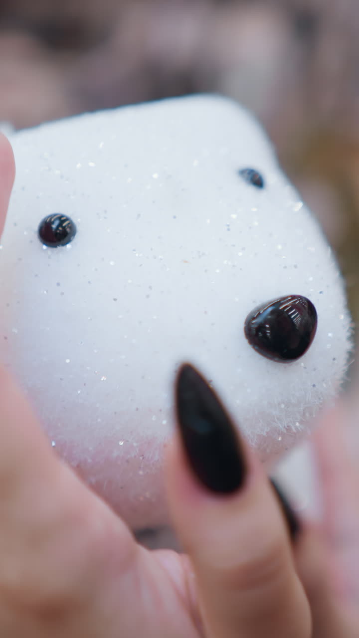 Close-up of a person's hand with black polished nails tenderly holding a white plush polar bear, highlighting the sparkling details against a softly blurred background