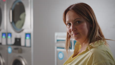 portrait of employer raising head with confident expression beside industrial washer and dryer inside laundromat, stainless steel polished, digital panels glowing, representing reliability, hygiene