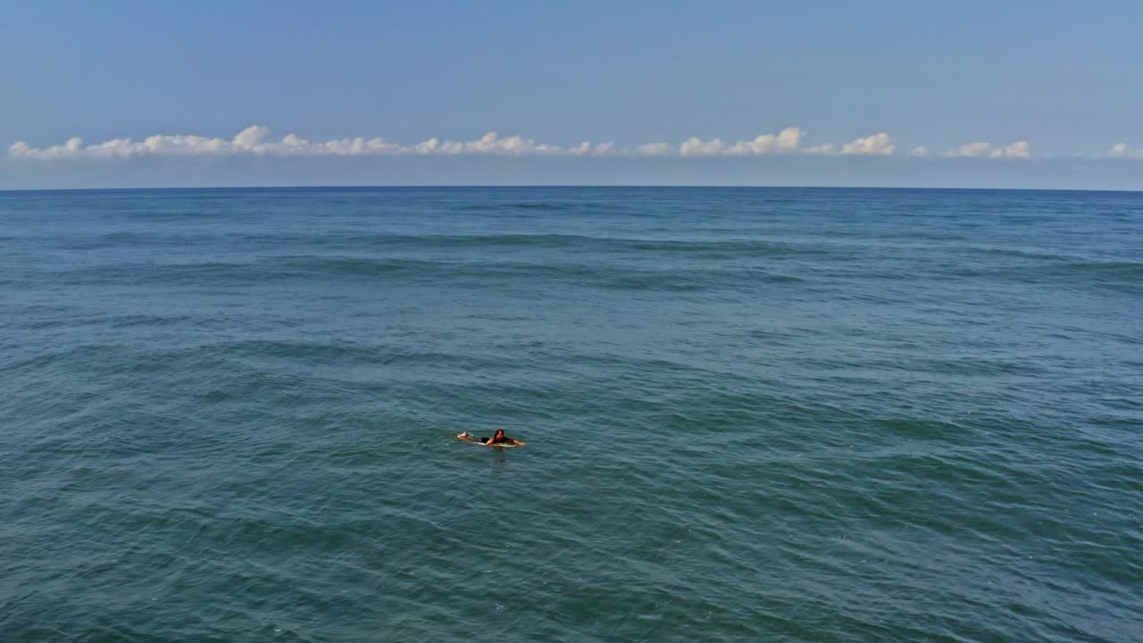 Surfer paddling over waves in tropical water, aerial view