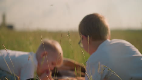 blurred close-up of two children lying on a checkered scarf in a grassy field, capturing a peaceful and serene outdoor moment. the children, dressed in white shirts, are nestled together