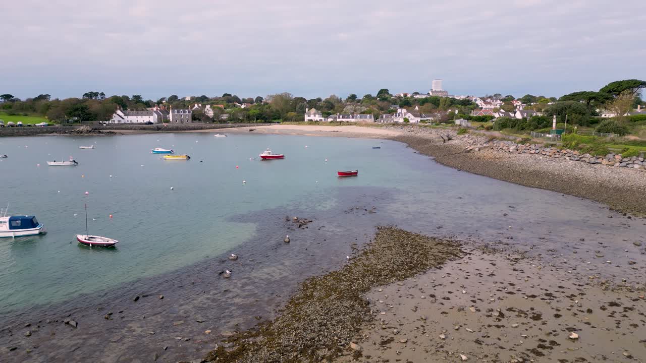 Lav flyvning over Bordeaux Havn Guernsey på vej mod kysten og stranden med både for anker på en lys eftermiddag med krystalklart vand.