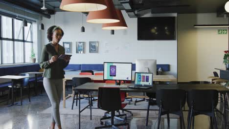 African-american-businesswoman-walking-and-using-tablet-alone-at-office