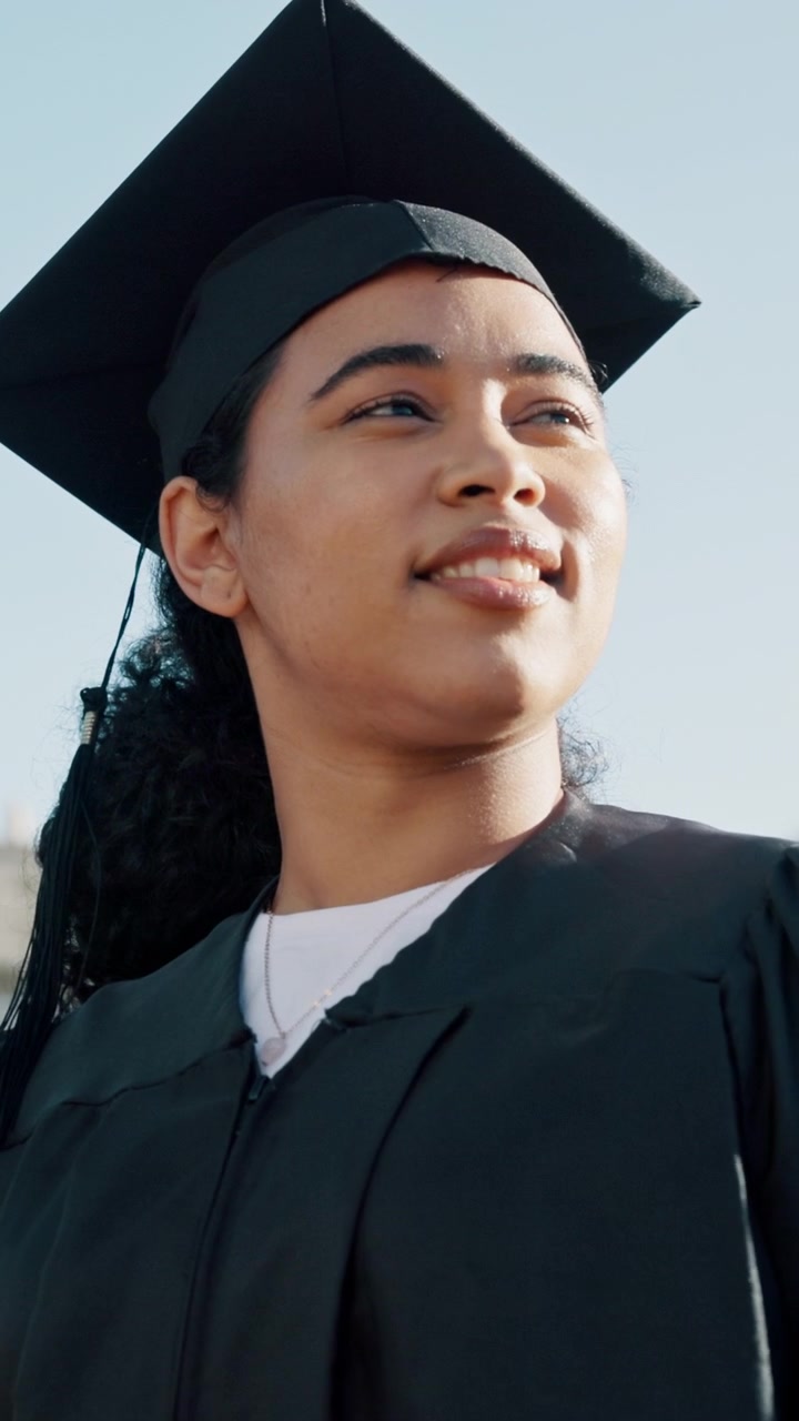 Giovane donna con tocco e toga da laurea che guarda verso il futuro