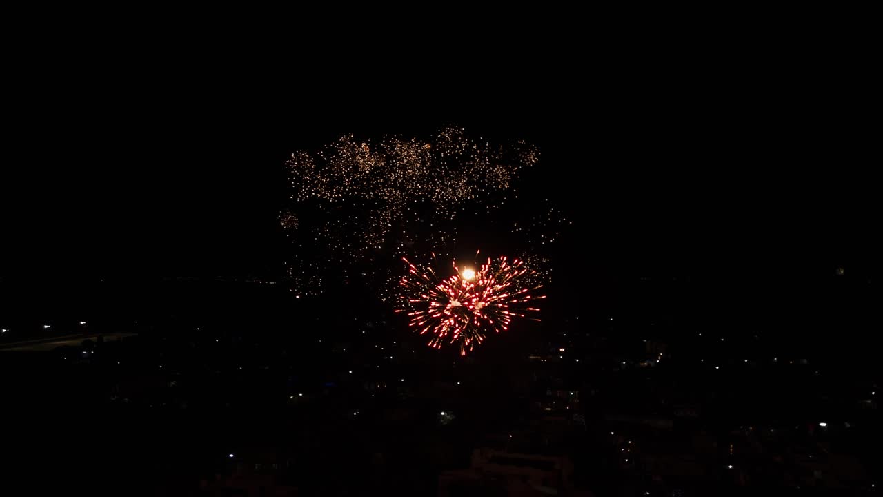 Colorful firework explosion lighting up dark night sky, bright spark trails and bursts, aerial static