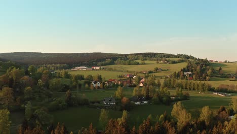 drone shot of czech highlands village surrounded with forest during sunset