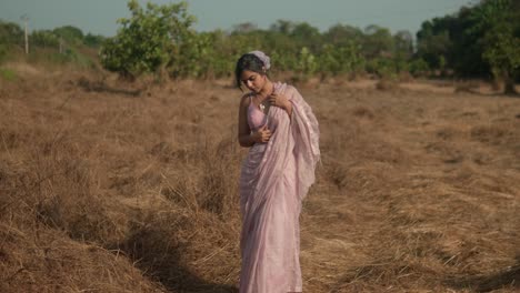 Frau-In-Rosa-Saree-Steht-Nachdenklich-Auf-Trockenem-Grasfeld,-Unter-Klarem-Himmel