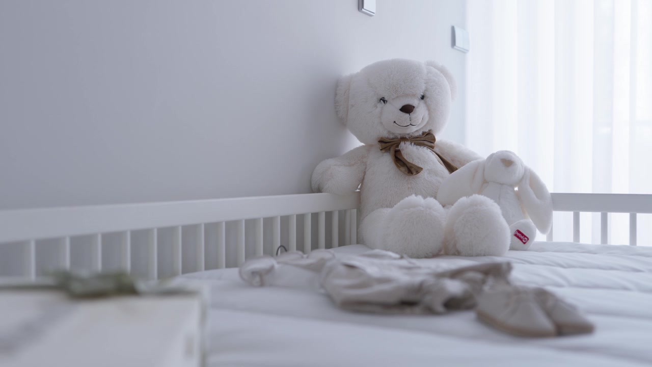 Teddy bear with bow and plush bunny sitting in a white baby crib with blanket
