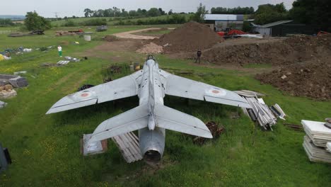 aerial view descending behind neglected hawker hunter fighter jet among discarded junk in field