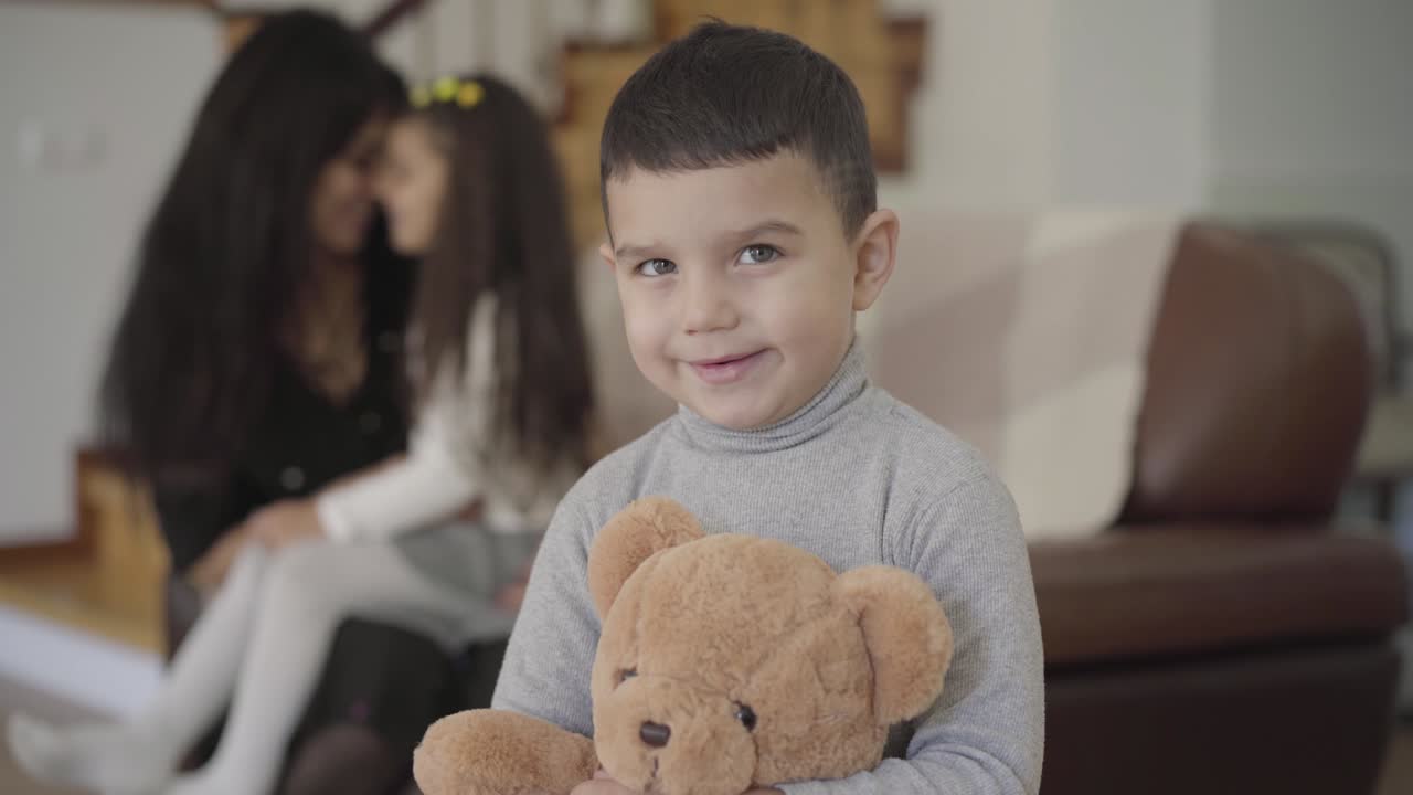 sonriente niño de oriente medio con ojos grises y cabello oscuro sosteniendo el oso de peluche y mirando a la cámara