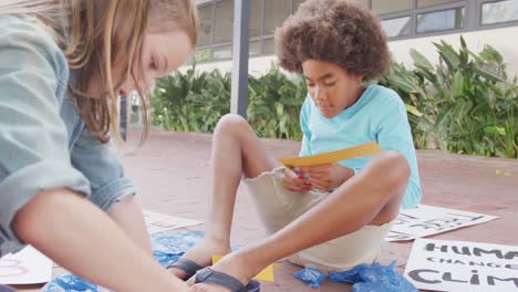 video of diverse boy and girl making protest placards in schoolyard, copy space