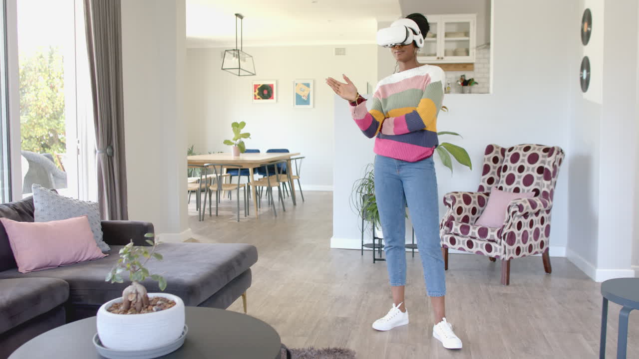 African American woman wearing virtual reality headset, standing in living room, at home, copy space