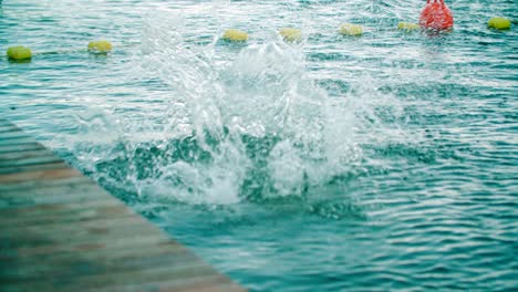 Low-Angle-Shot-Eines-Kaukasischen-Kindes,-Das-Von-Einem-Pier-In-Das-Wasser-Des-Sees-Springt