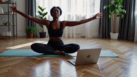 african american woman practicing yoga or meditation at home with laptop