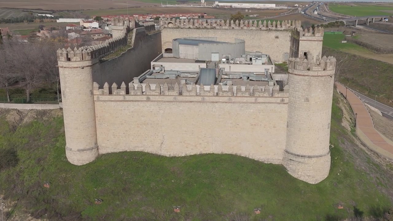 Droneflyvning forfra som nærmer seg Maqueda slott en solrik vintermorgen, og viser frem dens imponerende middelaldermurer, brystvern, indre gårdsplass og den omkringliggende landsbyen og grønne åkrene