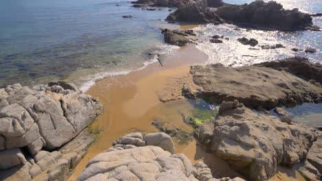 slow motion view of gently waves rolling into golden sand beach with large rocks