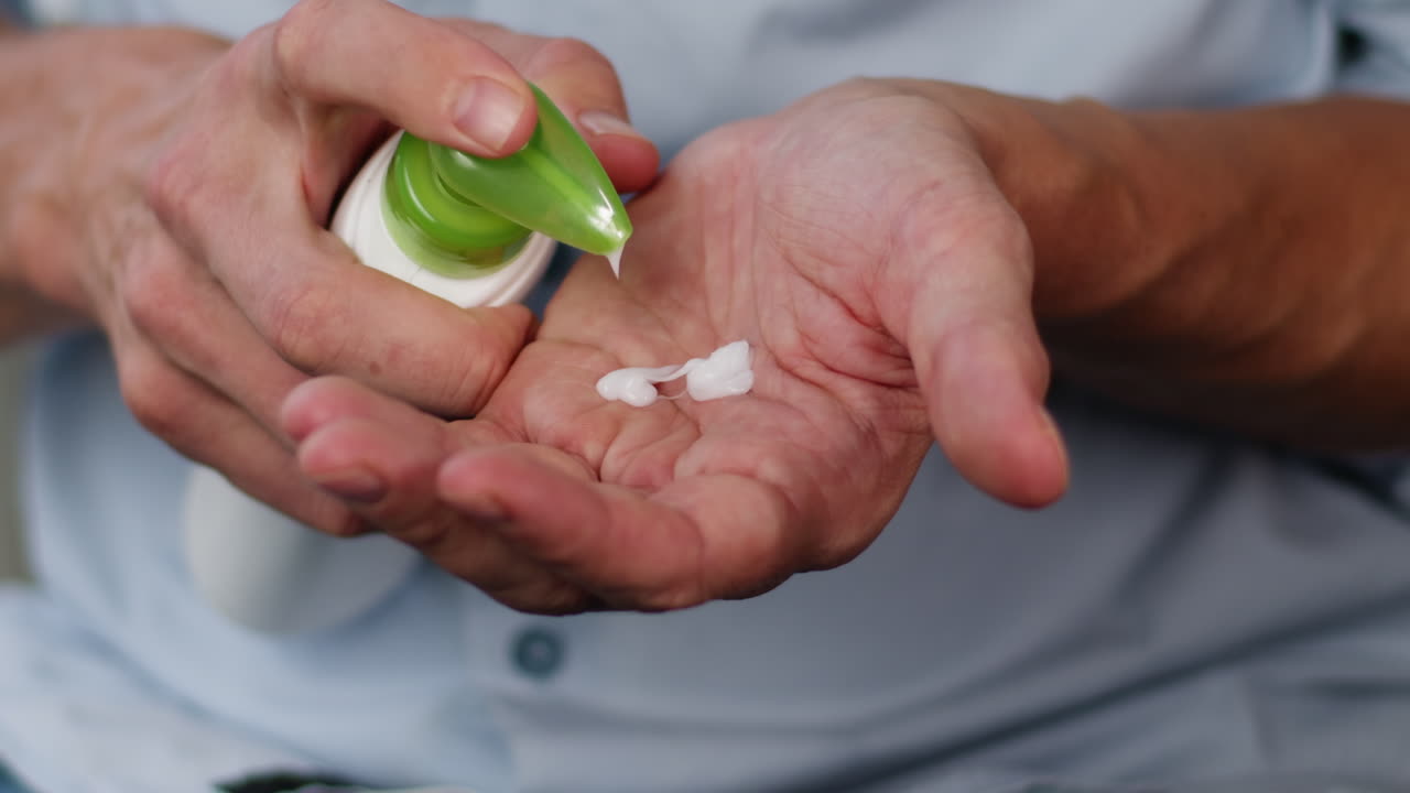 Young man squeezing a white moisturizer from a tube on his hand close-up. Morning routine. Beauty and care concept.