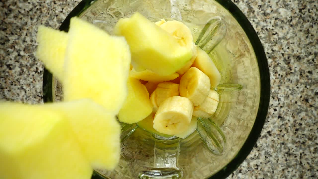Pezzi di mele cadono nel boccale di un frullatore su pezzi di banane. Movimento rallentato. Riprese in cucina. Vista dall'alto.
