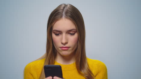 Retrato-De-Una-Mujer-Atractiva-Molesta-Usando-Un-Teléfono-Inteligente-Sobre-Fondo-Gris.