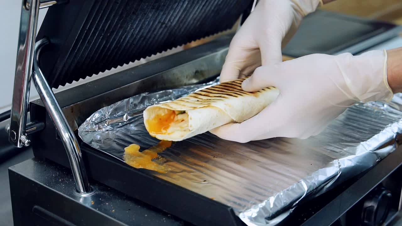 Grill fries shawarma. Cook takes out ready shawarma. Delicious pita in grilling machine. Baking pita in the restaurant. Cooking fast food